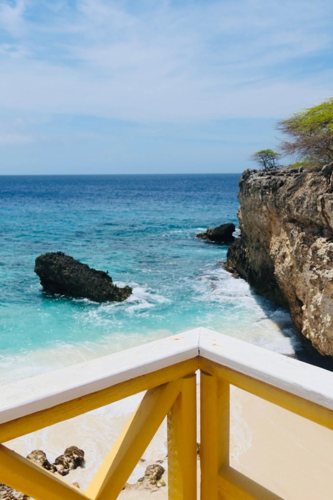 Uitzicht vanaf een balkon over een klif op een turquoise baai